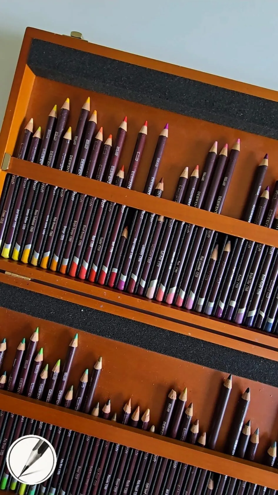 An open wooden box of coloured pencils arranged in tiered trays