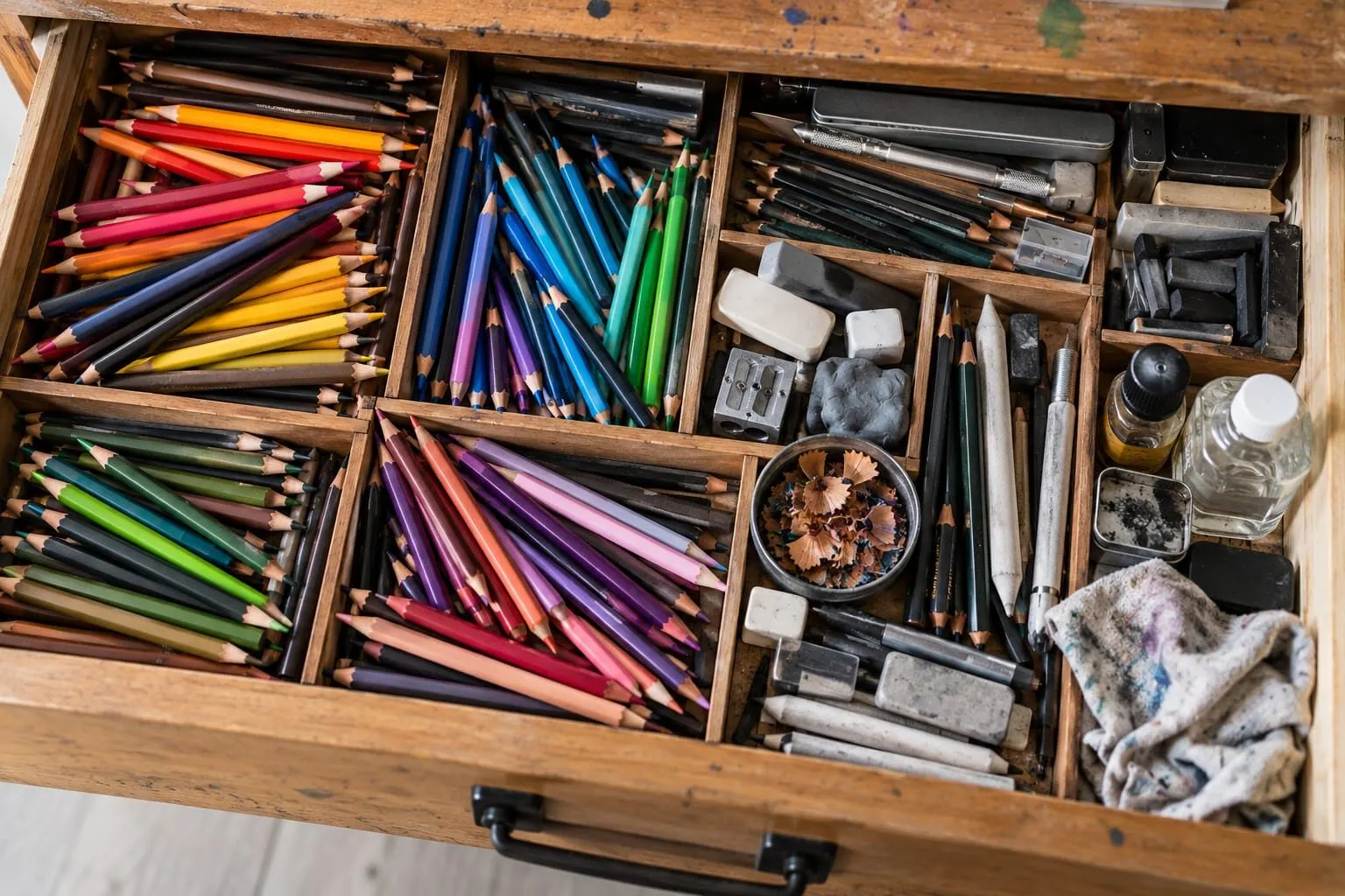 A wooden drawer of coloured pencils, erasers, brushes and art supplies in separate compartments